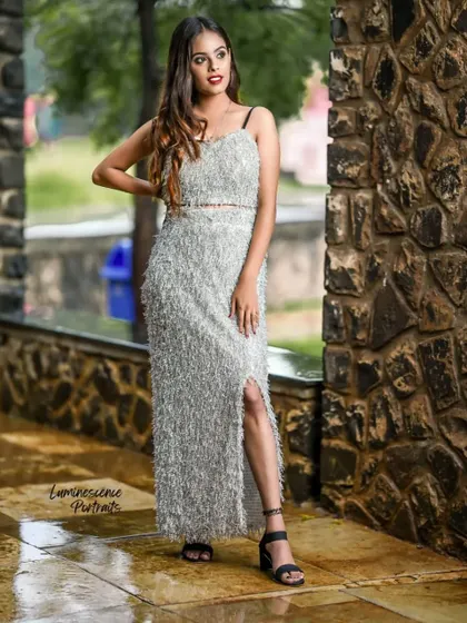 A confident pose in a striking silver outfit, with the model's hand on her hip, showcasing the dress's texture and side slit.