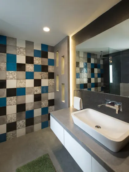 This contemporary bathroom in the Grey Apartment stands out with its vibrant checkerboard wall in tones of grey, blue, and black. A minimalist floating vanity with a backlit mirror blends functionality with bold design.
