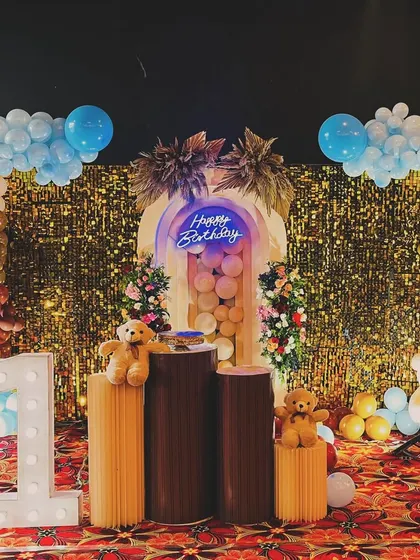 This setup features a stunning gold sequin wall with a 3D arch panel in the center. The decor is perfect for a glamorous teddy bear theme, using a mix of balloons and floral arrangements.