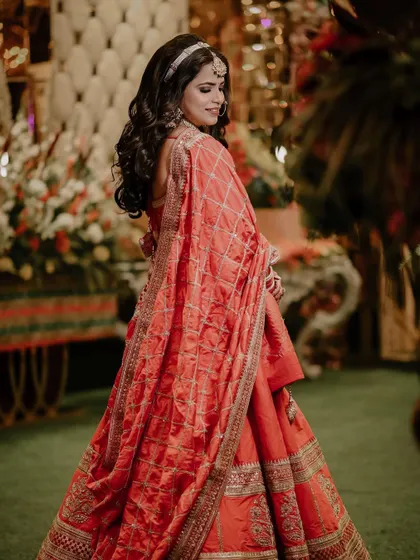 A full-length portrait of the bride, Reewa, in her beautiful orange wedding lehenga.