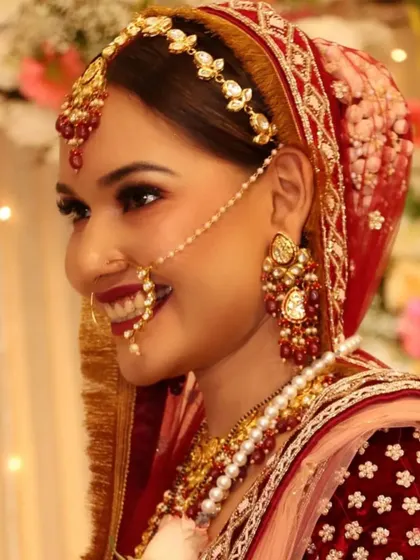 A happy bride smiling, showing off her classic red and gold themed makeup and jewellery.
