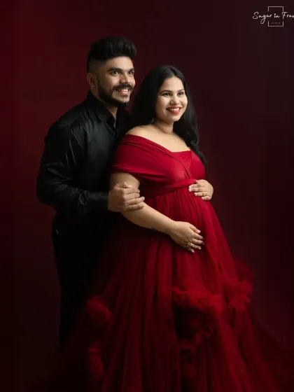 A joyful and elegant couple's portrait. Their bright smiles add a touch of warmth to the dramatic red backdrop and formal attire.