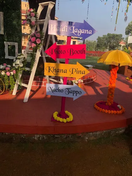 Fun and quirky signage is a must for a lively Haldi function. This colorful signpost directs guests to all the important spots: 'Haldi Lagana', 'Photo Booth', 'Khana Pina', and 'Nacho Tappo'.