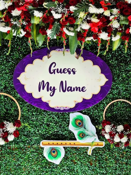 A detailed shot of the central part of our naming ceremony backdrop, showing the "Guess My Name" sign and the peacock feather and flute motif.