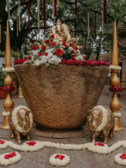 A close-up of a traditional decor element, featuring a large stone urli filled with flowers and guarded by small golden elephant statues.