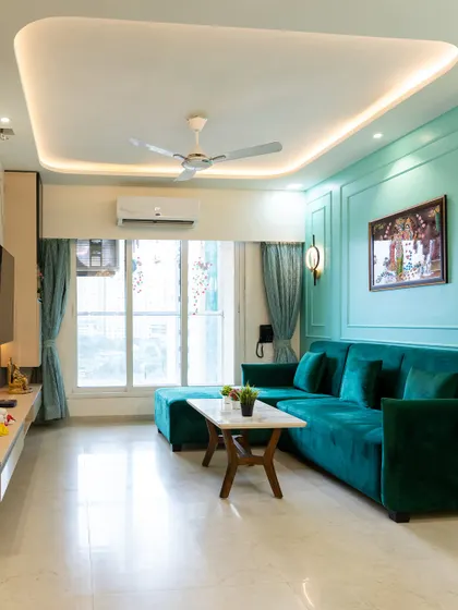 This living room combines a vibrant teal sectional sofa with matching wall color and a false ceiling with soft cove lighting, creating a bold yet harmonious look.
