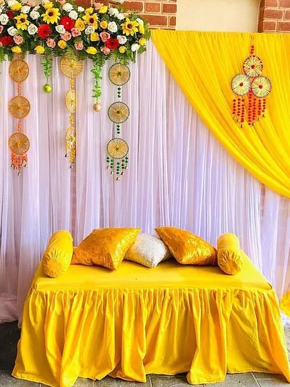 A simple and sweet Haldi setup. The combination of white and yellow drapes with colorful floral arrangements is both classic and beautiful.
