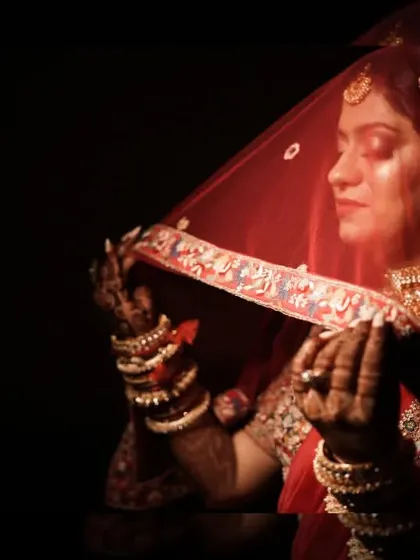 An artistic shot of the bride under her red veil, her hands framing her face. The focus is on her serene expression and the intricate details of her look.