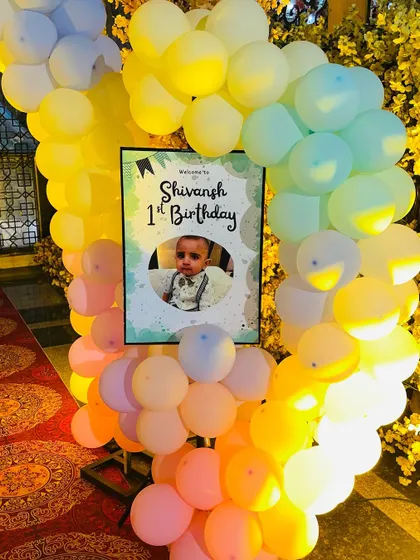 A personalized welcome sign for Shivansh's first birthday party. The sign is framed by a pastel rainbow balloon arrangement, setting a cheerful tone at the entrance.