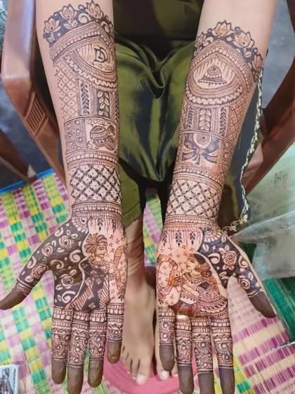 A stunning bridal mehendi with detailed portraits of a bride and groom. The design also includes auspicious symbols like the kalash and swastika, woven into the patterns on the arms.