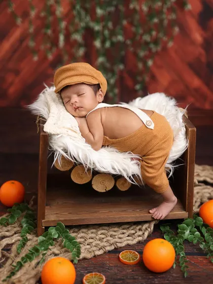 A newborn in a charming romper and cap, sleeping peacefully on a log-style prop. The surrounding oranges and greenery add a rustic, natural touch.