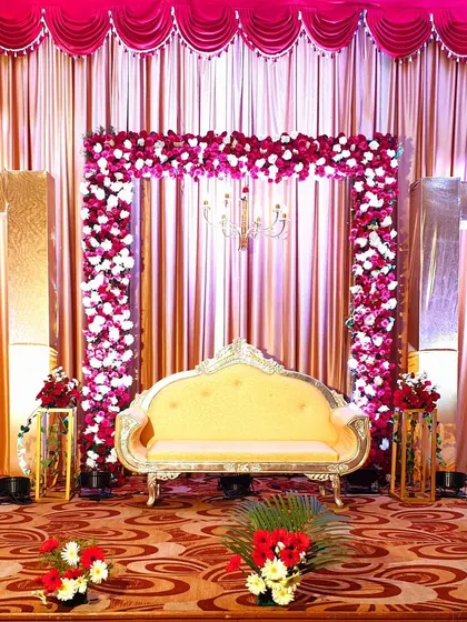 This is a full view of a grand reception stage, showcasing the interplay of the floral arch, shimmering curtains, and gold-framed side decor. The design creates a royal and festive atmosphere.