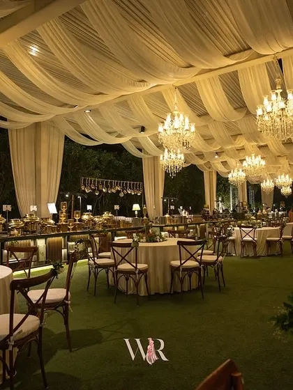 Another perspective of the grand outdoor dining area. The combination of the lush green lawn, the soft white table settings, and the warm light from the chandeliers created an atmosphere of pure elegance and sophistication.