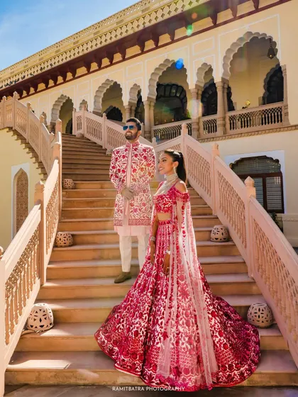 A full-length portrait of the couple on the steps of Rambagh Palace, showcasing their stunning Manish Malhotra outfits.