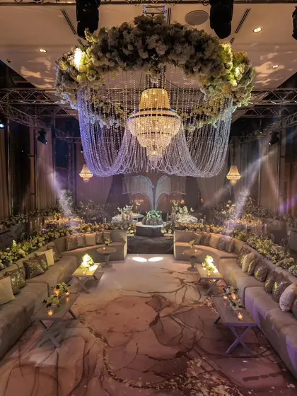 The gala night setup for a silver jubilee in Istanbul. A magnificent floral wreath and chandelier hang over a circular lounge seating, creating a space that is both grand and intimate.