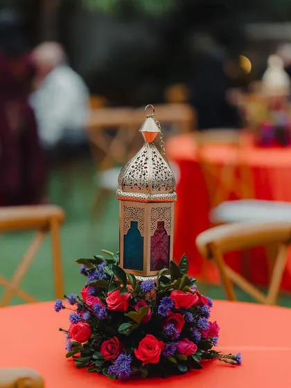 A Moroccan lantern serves as a unique centerpiece on a guest table, surrounded by a ring of colorful flowers.