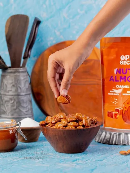 A simple, clean shot featuring a hand model picking up a nutty almond. This style of photography helps customers visualize themselves enjoying the product, making it more relatable.