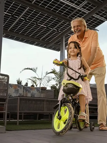 A grandfather helps his granddaughter ride her bicycle under the shade of their new solar panel structure. Our systems are built to protect what matters most, your home and your family.