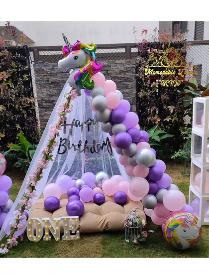 An outdoor unicorn-themed teepee setup, perfect for a garden party. The decoration includes a unicorn foil balloon, pastel balloon garland, and 'ONE' marquee letters.