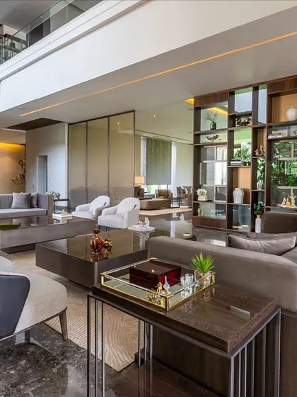 In this double-height living area, furniture is used to create human-scaled spaces. The arrangement of sofas and console tables helps to ground the room, while the open-backed shelving unit adds vertical interest without obstructing the view.