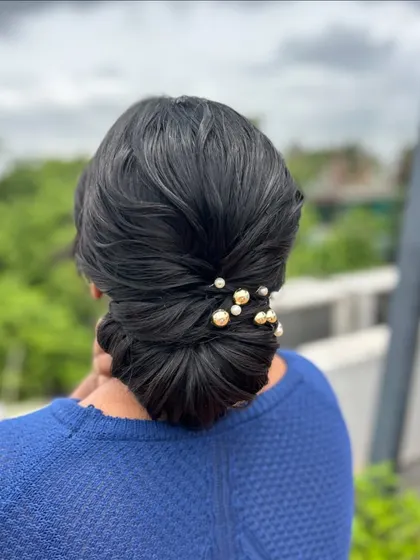 A clean, classic low bun with a simple twist detail, adorned with elegant pearl and gold pins. This timeless style is a must-know for any hairstylist.