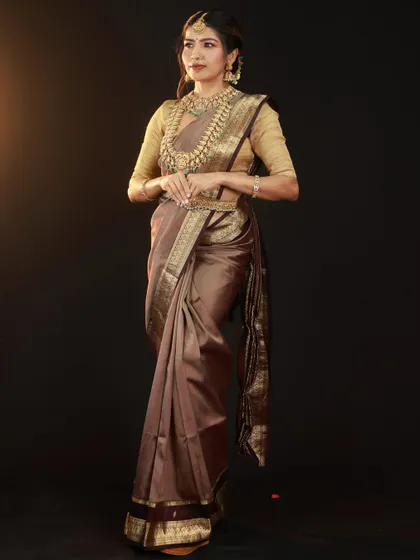 A full-length portrait to showcase the beautiful drape and fall of the brown silk saree. The side lighting adds depth and highlights the texture of the fabric.
