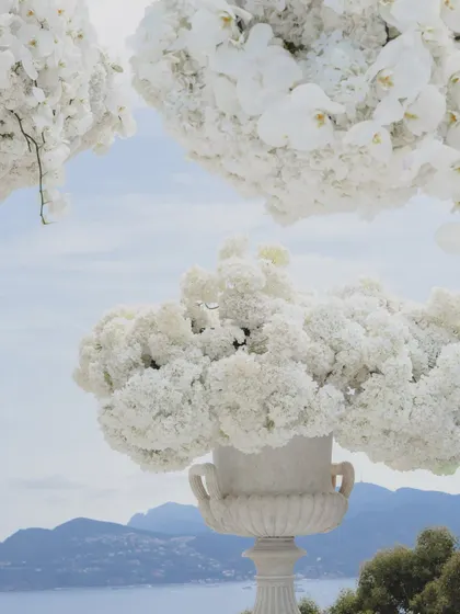 A close-up of the massive floral arrangements in classic stone urns, filled with clouds of white hydrangeas and orchids, overlooking the French Riviera.
