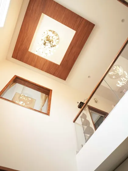 A view from the lower level looking up at the double-height ceiling, featuring a wooden-clad ceiling detail and a modern chandelier.