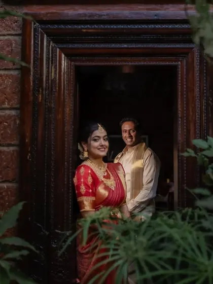 A portrait of the bride in her stunning red saree, framed by the rustic charm of her wedding venue. We focus on creating images that are both beautiful and full of character.