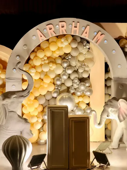 A grand backdrop for Arrham's first birthday, featuring elephant props and a large arch filled with yellow and silver balloons.