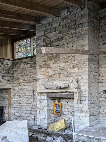 The interior stone walls and fireplace of a Himalayan guesthouse take shape. The massive stone chimney serves as the thermal heart of the home, providing warmth while anchoring the living space.