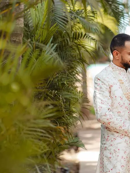 The couple shares a sweet look amidst lush greenery. The natural framing provided by the palm leaves adds depth and focuses the viewer's attention on their interaction.