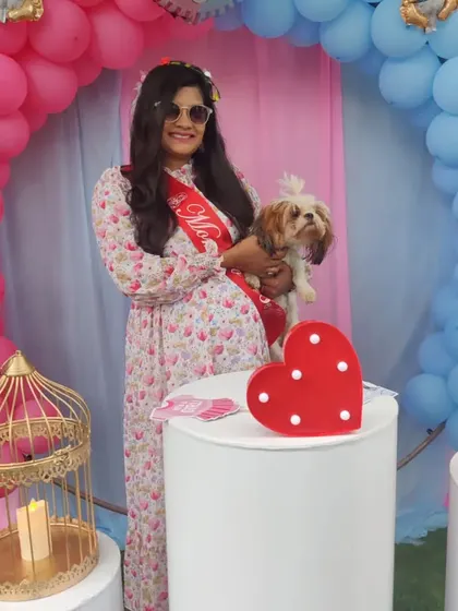 A heartwarming moment from a baby shower we decorated. The mother-to-be poses with her pet in front of the pink and blue balloon arch, showing how our decor sets the scene for special memories.