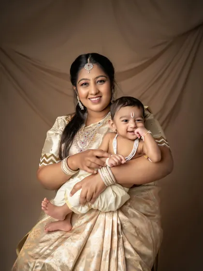 A mother's love shines through in this beautiful portrait with her little Krishna. The coordinated golden sarees and dhotis create a cohesive and elegant look for the whole family.