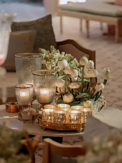 A close-up of a table centerpiece featuring lotus pods and white flowers, surrounded by candles. The warm, ambient lighting creates an intimate and serene atmosphere.