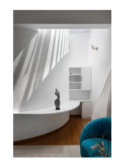 A skylit study nook carved out of a curved wall. The minimal white palette creates a serene and focused workspace, enhanced by the natural light from above.