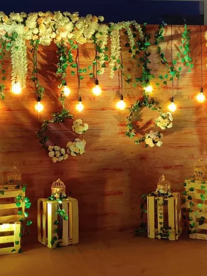 A rustic photo backdrop perfect for a beachside event. We used a wooden wall decorated with white flowers, greenery, and hanging Edison bulbs, with illuminated crates adding to the charm.