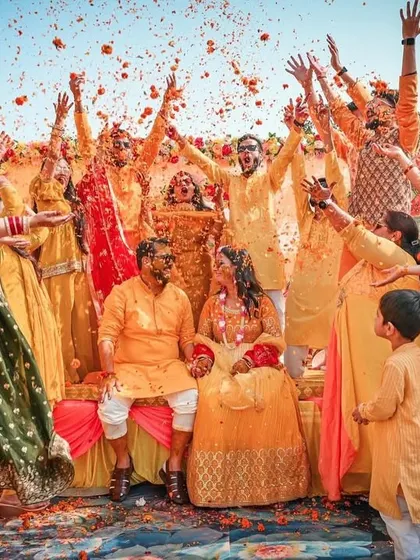 A wedding is about joy and celebration, and we capture every bit of it. This photo from a Haldi ceremony shows the couple surrounded by family and friends in a fun, candid moment of celebration, showering them with flower petals.
