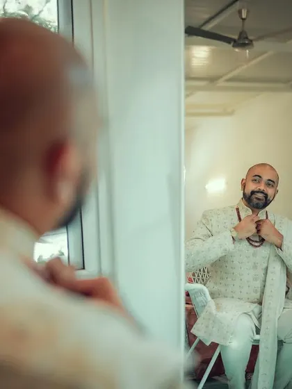 The groom getting ready, seen through his reflection in the mirror. A classic shot capturing the anticipation of the wedding day.