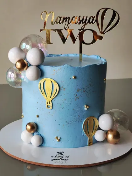 A dreamy hot air balloon-themed cake for a second birthday. The soft blue buttercream is decorated with gold and white balloons for a light and airy feel.