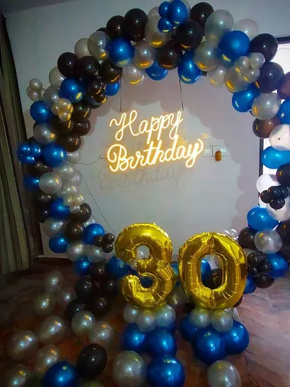 A stylish ring backdrop for a 30th birthday. The circular frame is decorated with blue, black, and silver balloons, with a central neon sign and large gold "30" foil numbers.