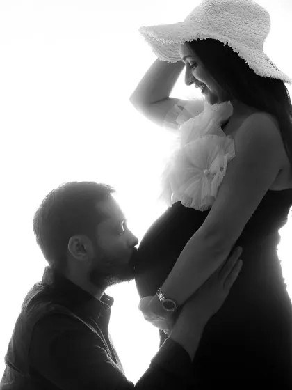 A beautiful black and white silhouette shot. The partner's kiss on the bump is a classic, tender moment, and the hat adds a touch of style.