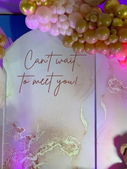 A close-up of the "Can't wait to meet you!" backdrop with a pink and gold marble effect.