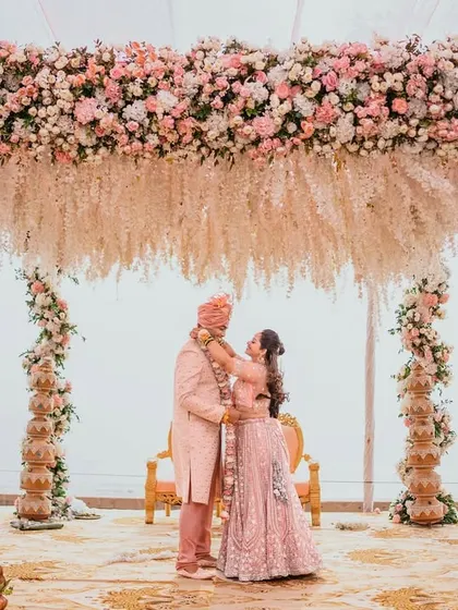 A wide shot of the couple under a breathtaking floral mandap during their Hindu wedding ceremony. This image showcases the grandeur of the decor and the intimacy of the couple's embrace.
