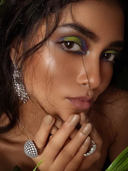 A close-up beauty shot with colorful, artistic makeup and statement diamond rings.