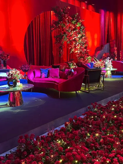 A close-up of a lounge area at the red-themed Sangeet, with a floral arrangement and a bed of roses illuminated by fairy lights, creating a magical and romantic detail.