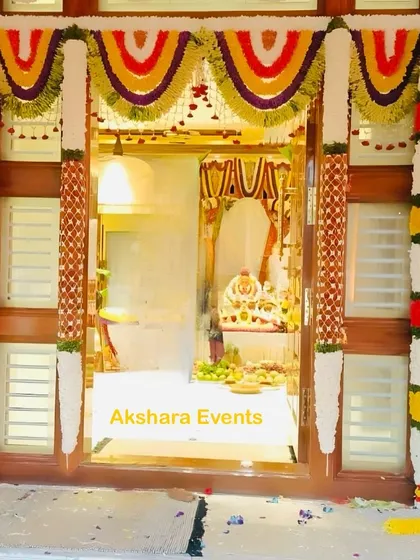 A traditional floral decoration for a housewarming ceremony. The main door is beautifully framed with garlands of colorful flowers, creating a warm and festive welcome.