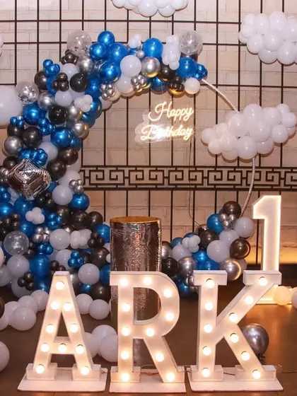 A celestial-themed first birthday for "Ark". The setup includes a balloon moon, balloon clouds, and light-up marquee letters.