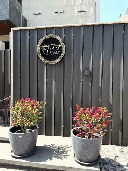 A custom nameplate on a modern slatted wall, flanked by two pots of vibrant bougainvillea, adding a personal touch and a splash of color.