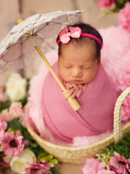 So delicate and sweet, this newborn girl is swaddled in pink and holds a tiny lace parasol, surrounded by a bed of flowers for a soft, romantic feel.